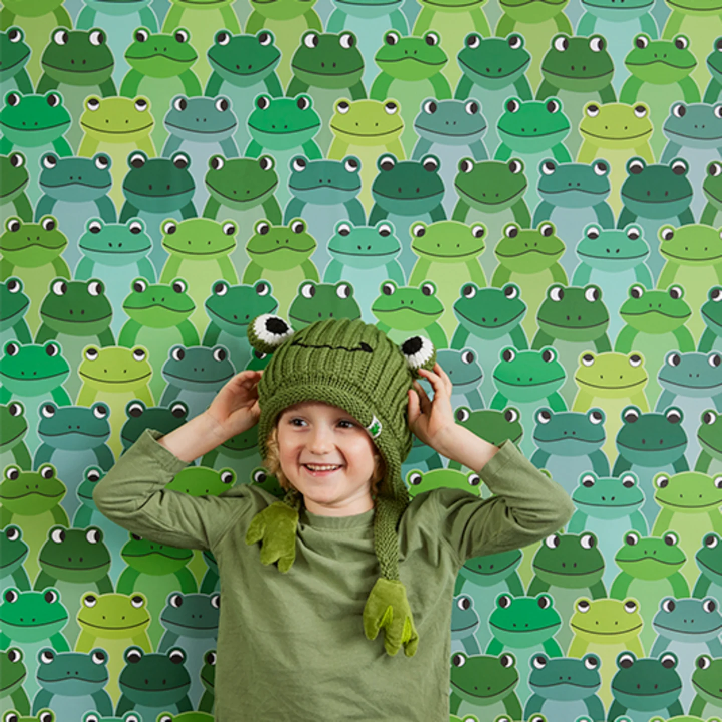 Boy with frog hat next to frog wallpaper.