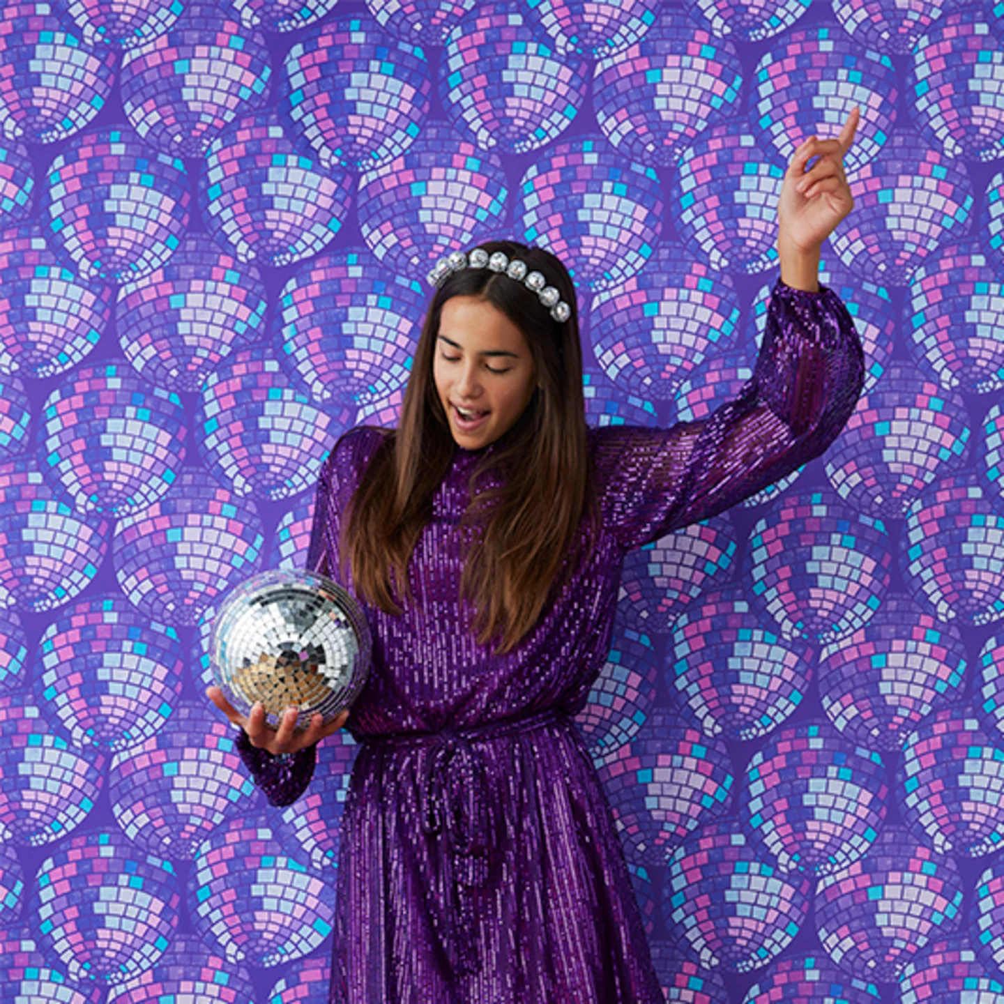 Girl in sparkly dress and disco ball next to purple disco ball wallpaper.