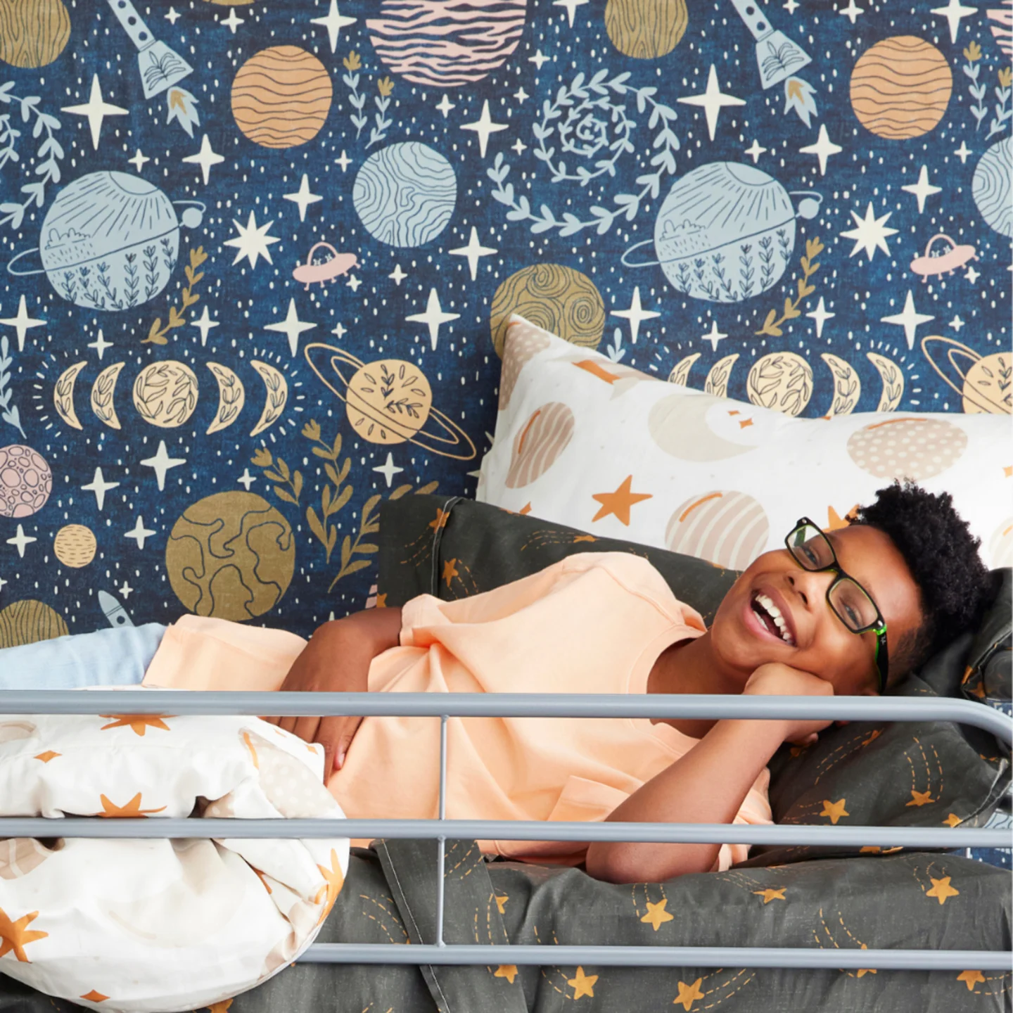 Boy in bunk bed with space wallpaper.